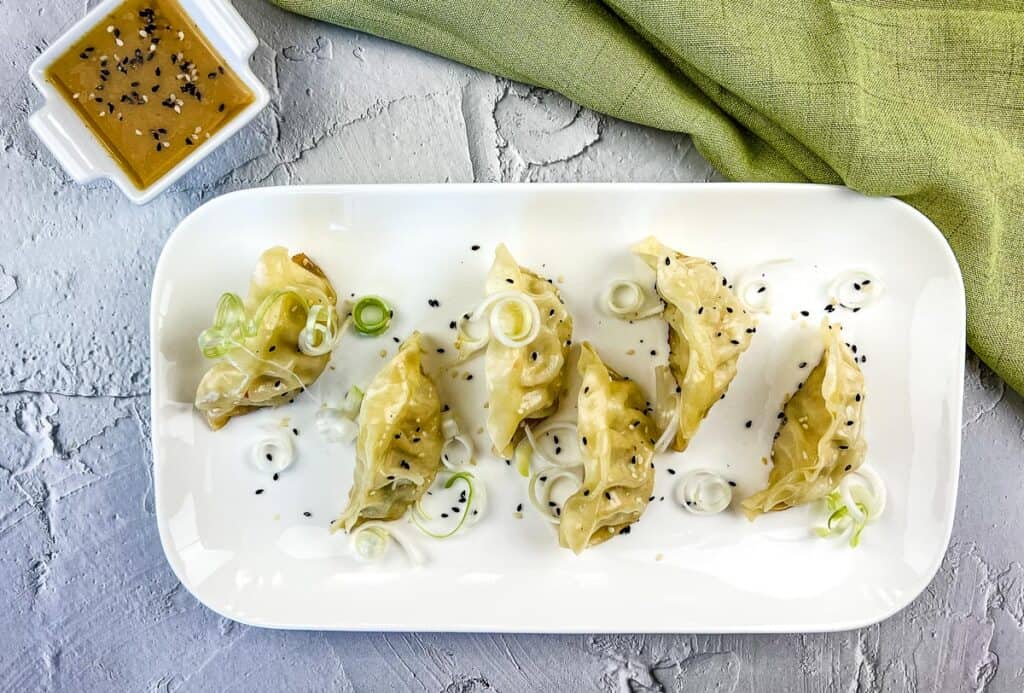 Potstickers on the Blackstone served on a white platter with sauce.