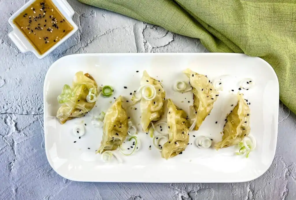 Potstickers on the Blackstone served on a white platter with sauce.
