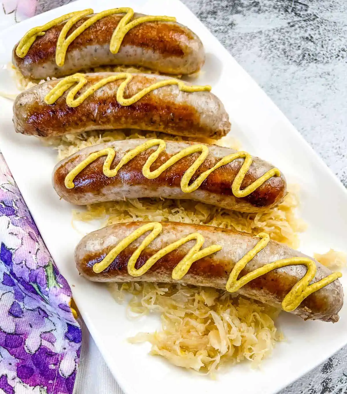 sausage with mustard on top of sauerkraut on a white platter