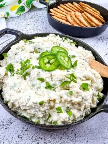 A closeup image of artichoke jalapeno dip in a black dish with crackers in the background.