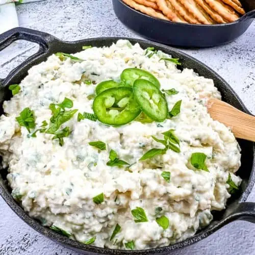 A closeup image of artichoke jalapeno dip in a black dish with crackers in the background.