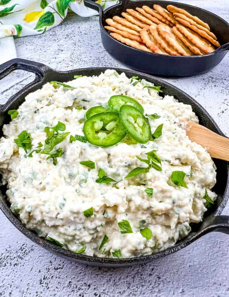 A closeup image of artichoke jalapeno dip in a black dish with crackers in the background.