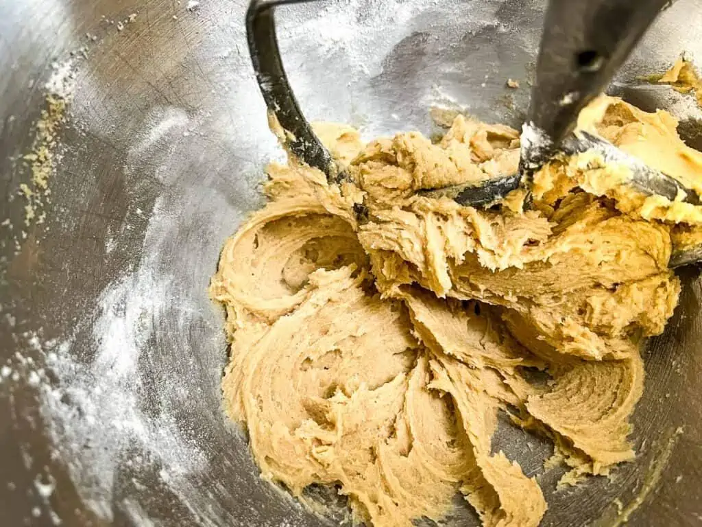 Cookie dough for air fryer oatmeal raisin cookies being mixed in a metal bowl with a stand mixer attachment visible.