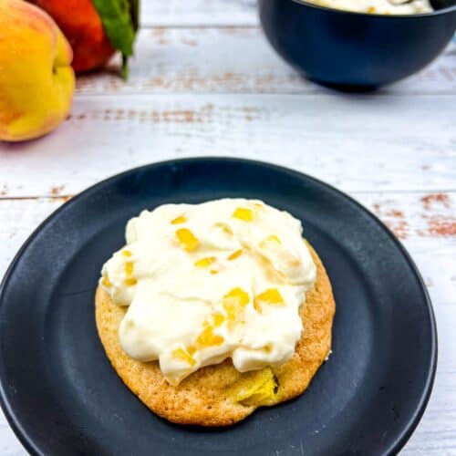 peaches and cream cookie on a black plate with peaches in the background.
