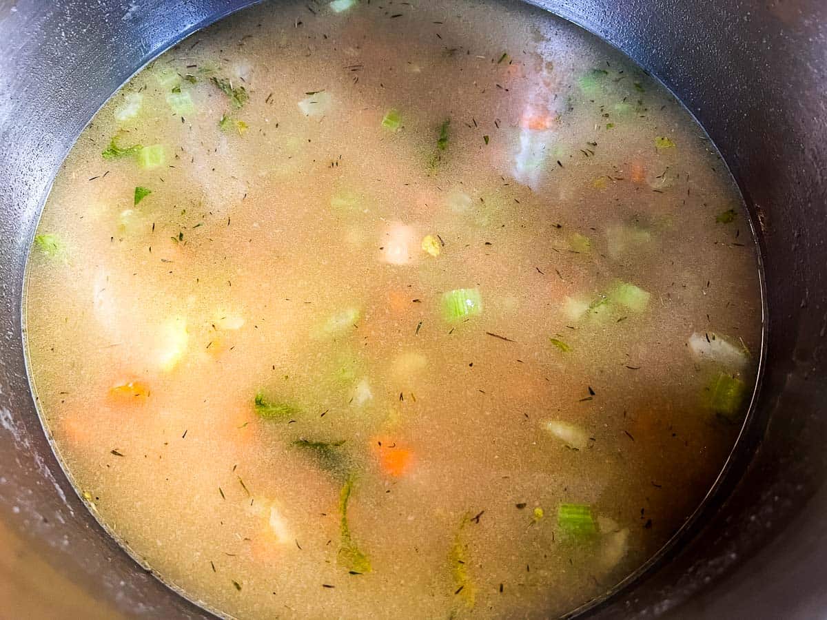 Adding broth and milk to the veggies in the soup pot.