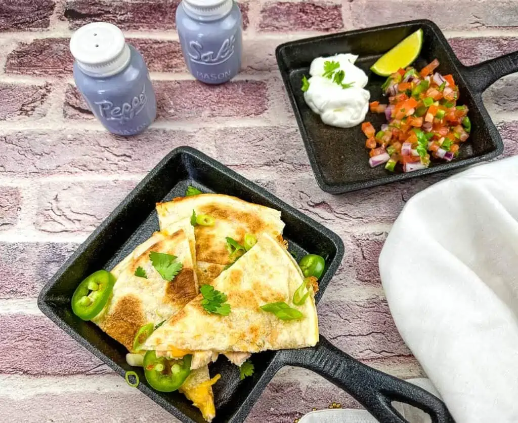 Smoked turkey quesadilla in a black skillet with pico de gallo in the background.