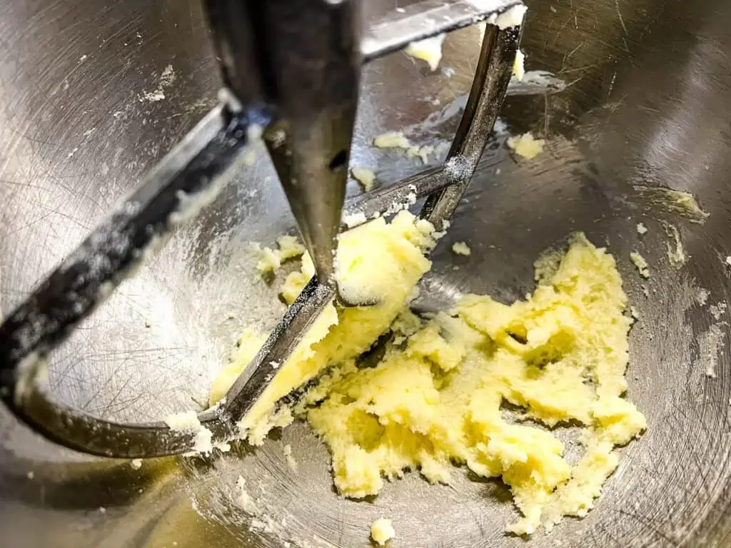 Butter and sugar are being creamed together in a metal mixing bowl with a stand mixer paddle attachment, forming the perfect base for zucchini cookies with chocolate and pecans.