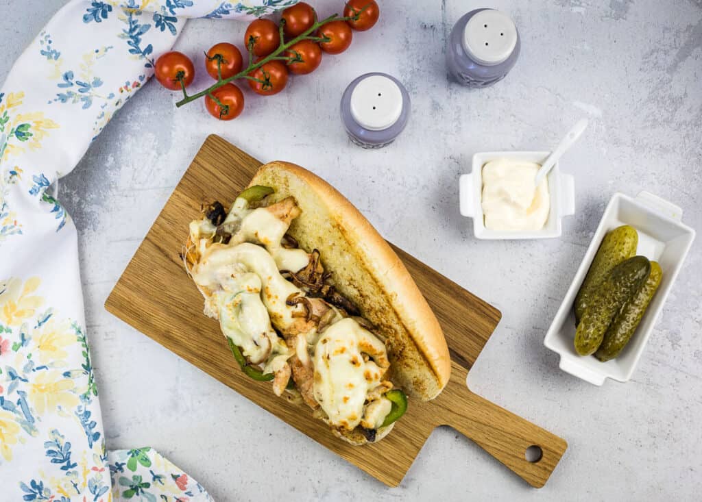 Top down shot of a blackstone chicken philly sandwich with pickles and tomatoes nearby.