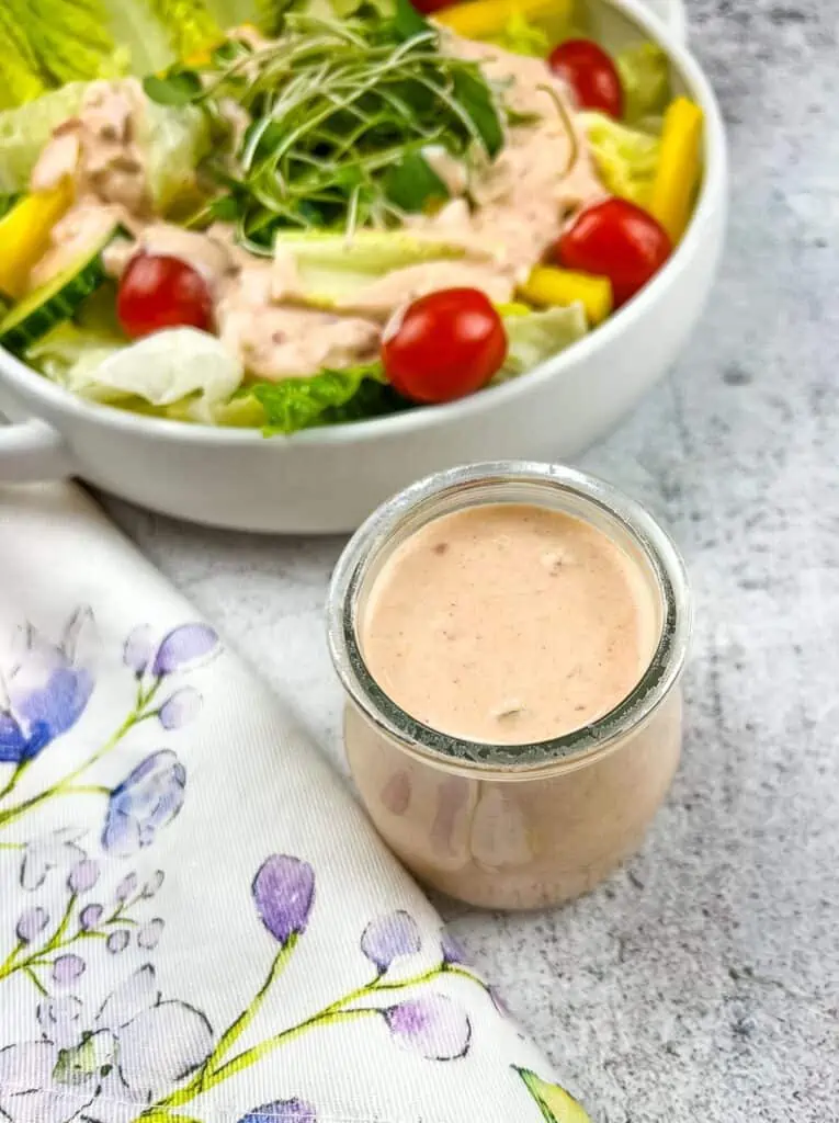 Russian dressing in a jar with a salad in the background.