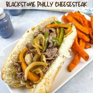 Philly cheesteak sandwich with sweet potato fries on a plate.