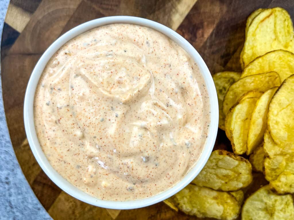 A bowl of dip with chips around it.