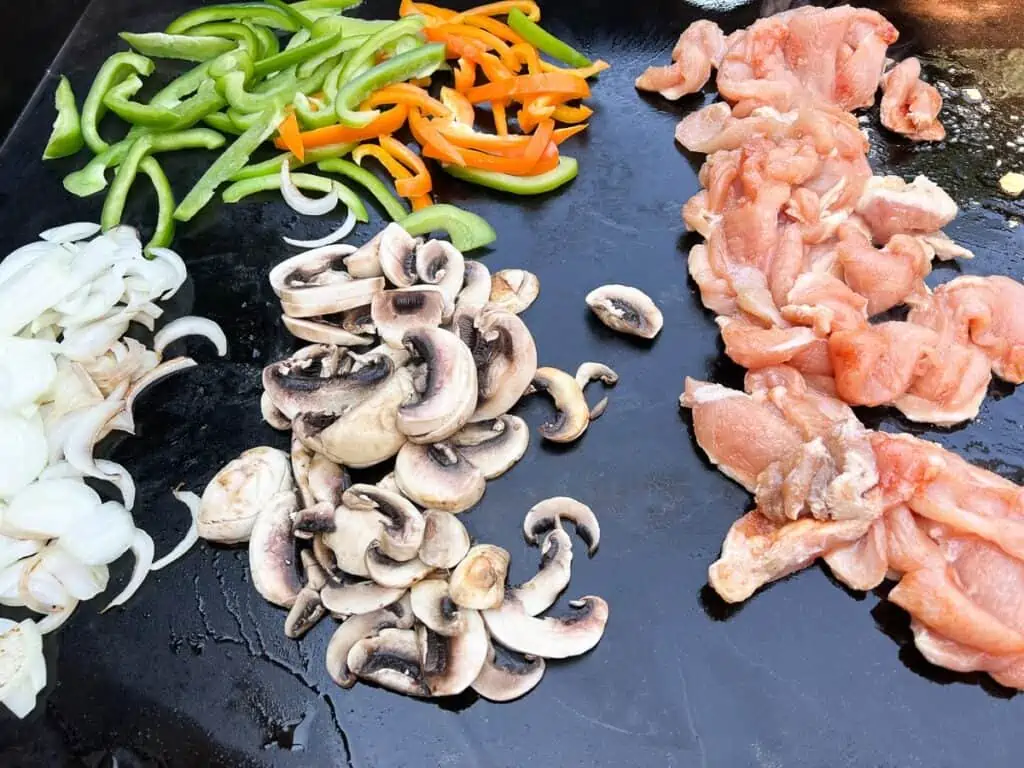 Cooking the onions, peppers, mushrooms, and chicken in different spots on the griddle.