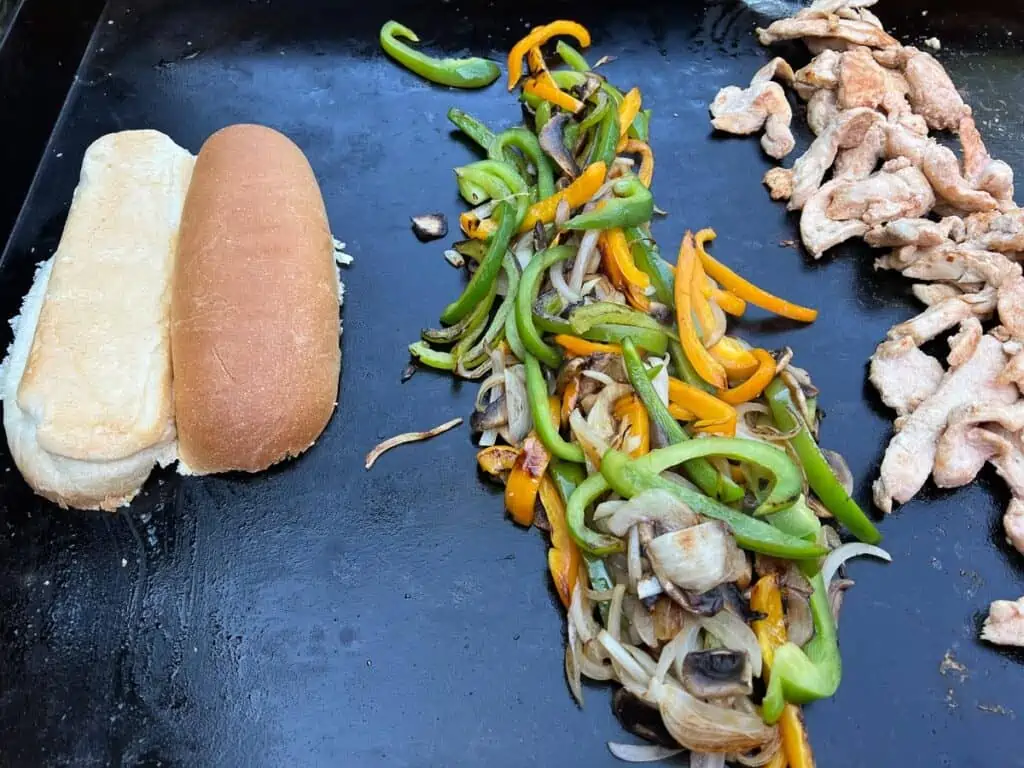 Combining the cooked veggies and toasting a bun to make Blackstone Chicken Philly Cheesesteaks.