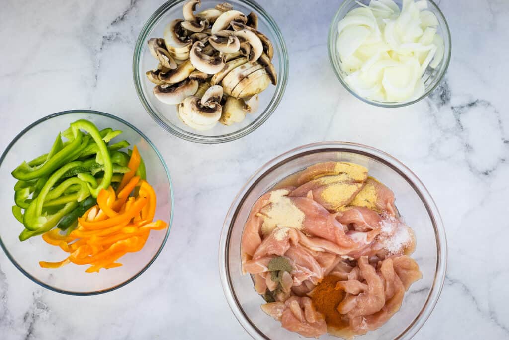 Sliced onions, peppers, and mushrooms, and a bowl with the chicken and spices.