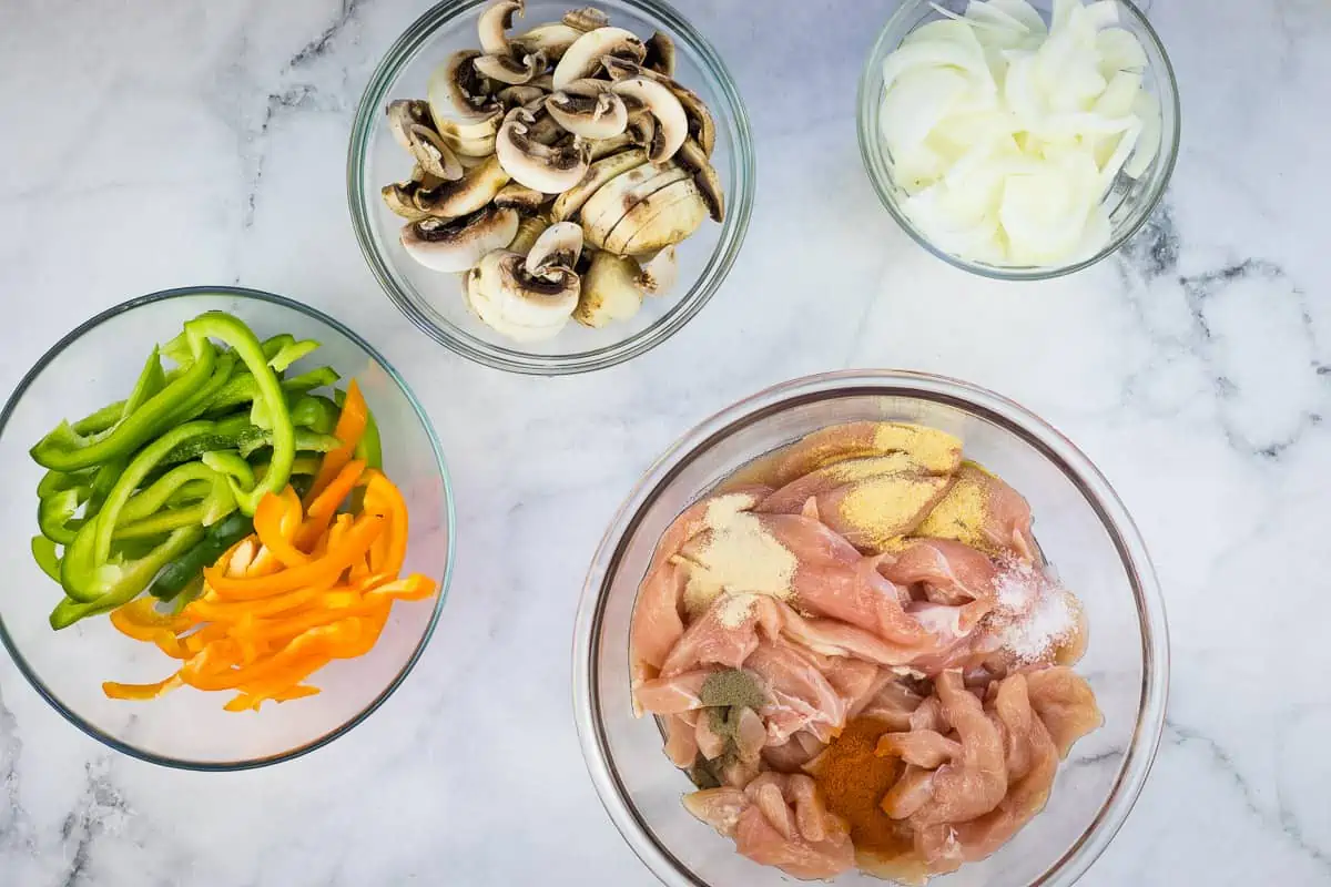 Sliced onions, peppers, and mushrooms, and a bowl with the chicken and spices.