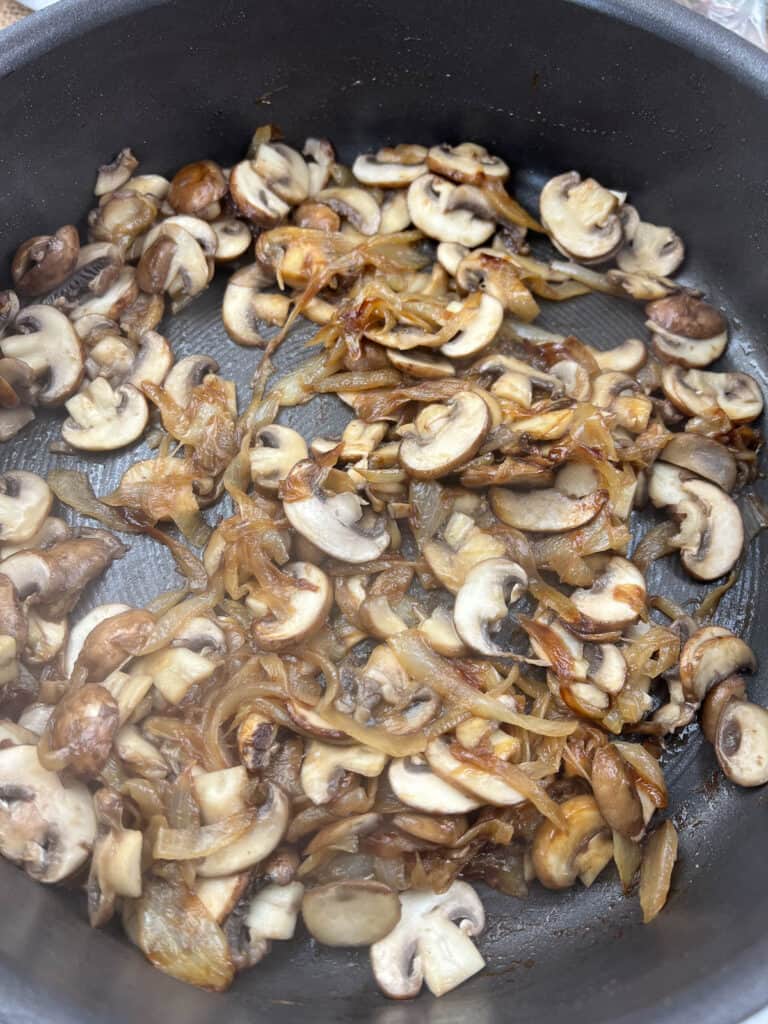 Mushrooms cooking in a skillet with the onions.