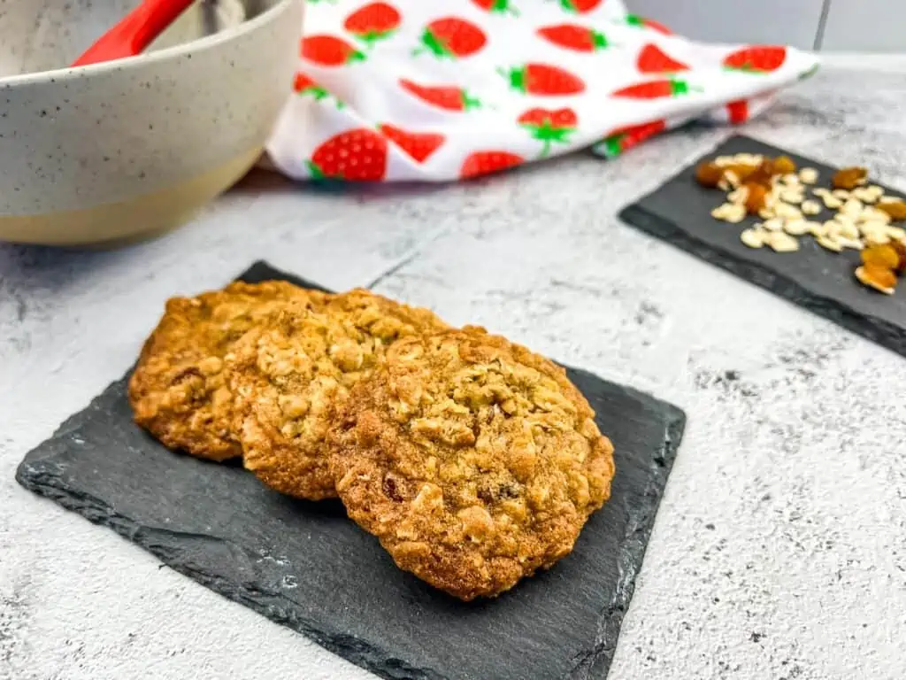 Two oatmeal raisin cookies on a slate board with strawberries.