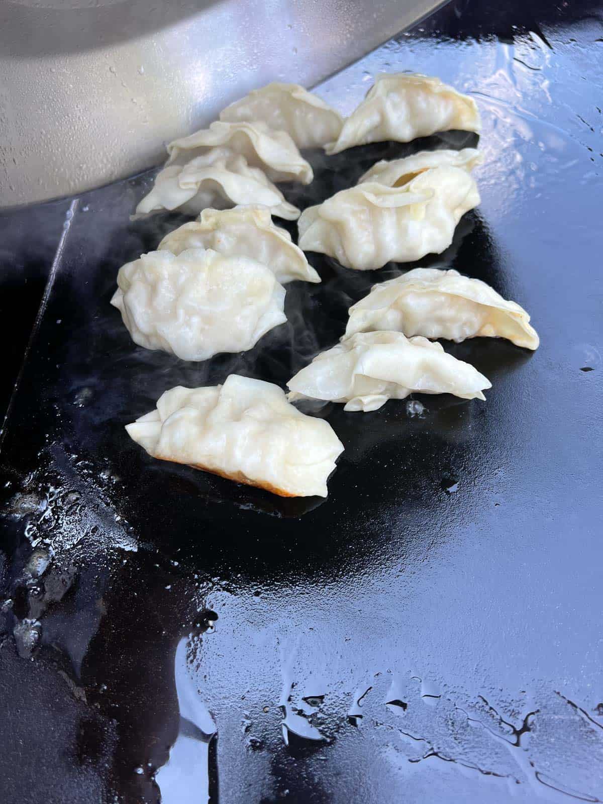 Adding water under the cooking dome to steam the potstickers.