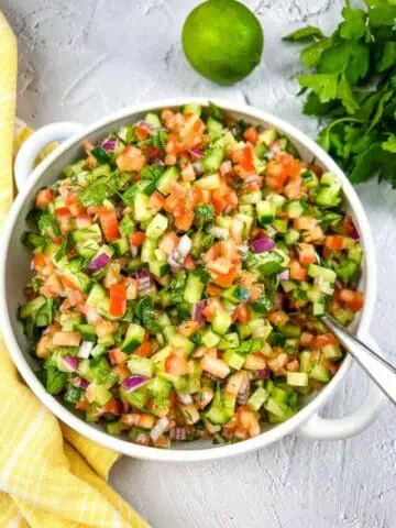 Shirazi Salad in a white bowl with parsley and lime in the background.