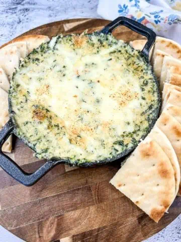 Spinach and Brie Dip in a cast-iron dish with pita chips around it.