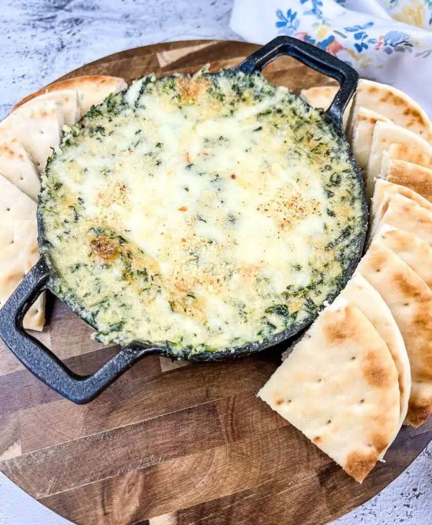 Spinach and Brie Dip in a cast-iron dish with pita chips around it.