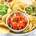 A closeup of pico de gallo and other salsas on a platter with tortilla chipos.