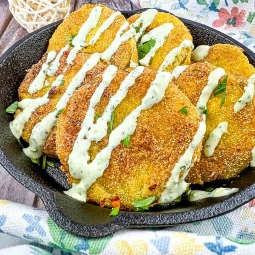 Fried tomatillos on a black plate drizzled with cilantro-jalapeno aioli.