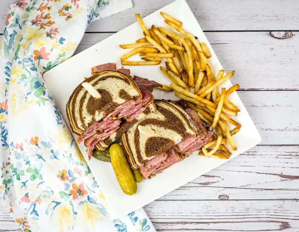 A top-down shot of a pastrami sandwich on marble rye with fries on the plate.