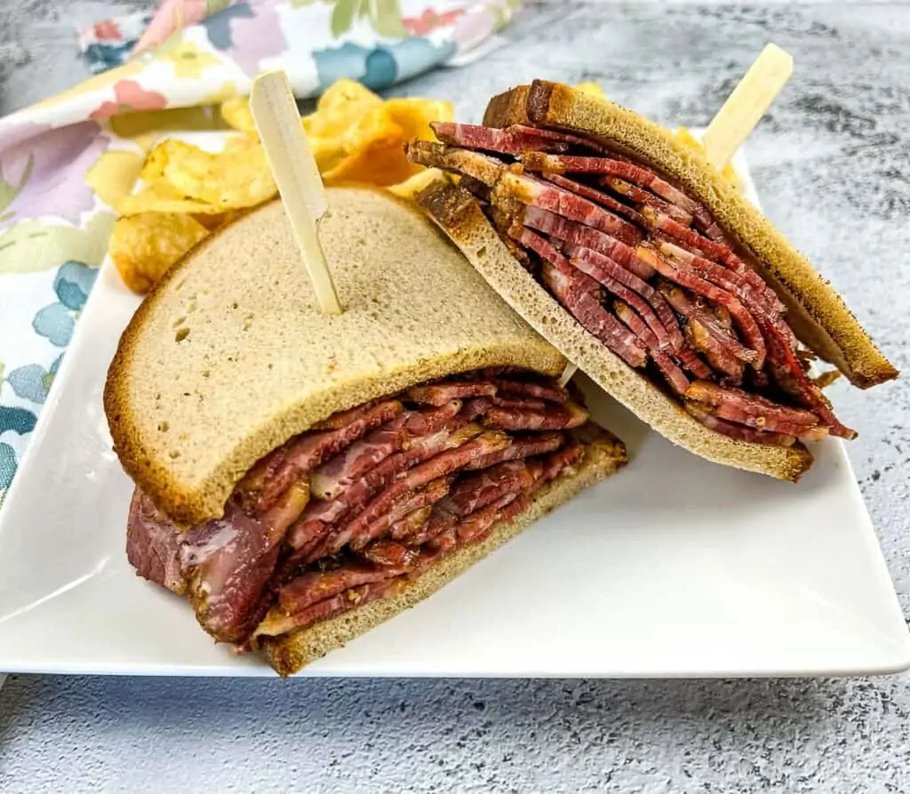 Homemade pastrami sandwich on rye bread with chips in the background.