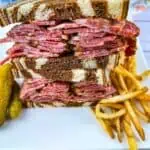 Pastrami sandwich on a white plate with fries.