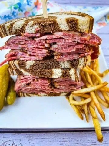 Pastrami sandwich on a white plate with fries.