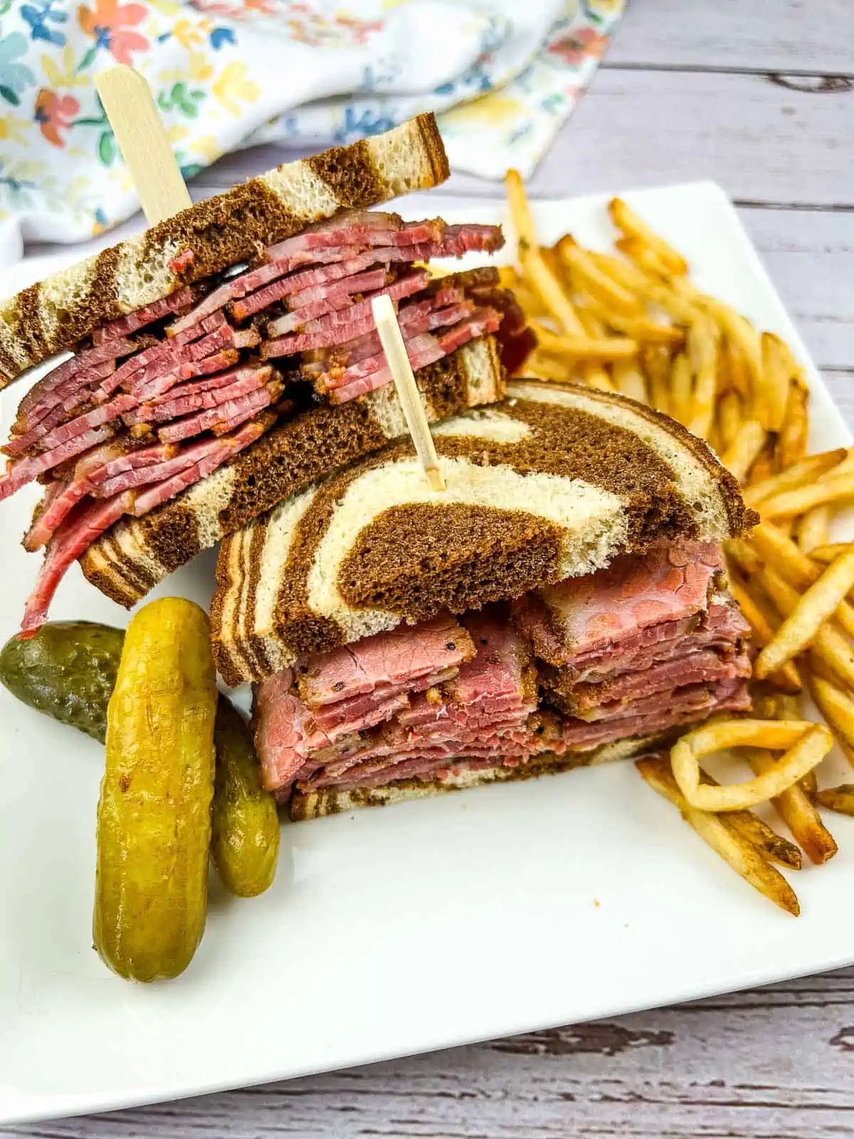 A homemade pastrami sandwich on marble rye with fries on the plate.
