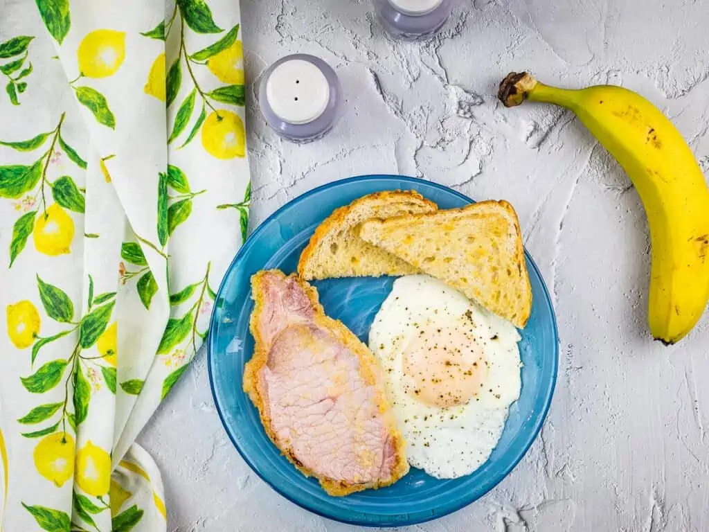 peameal bacon on a blue plate with toast and eggs.