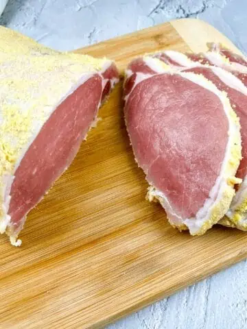 Cured and sliced raw peameal bacon on a cutting board.