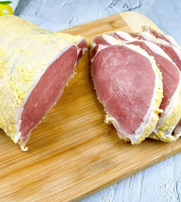 Cured and sliced raw peameal bacon on a cutting board.