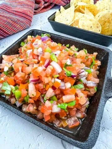 Pico de gallo in a black dish with tortilla chips in the background.