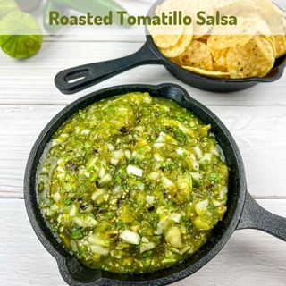 Roasted tomatillo salsa in a black serving dish with chips in the background.