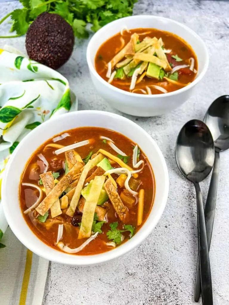 Smoked chicken tortilla soup in two soup bowls with spoons nearby.