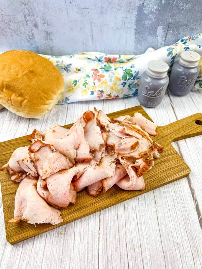 Sliced Smoked Pork Lunch Meat on a cutting board with buns in the background.