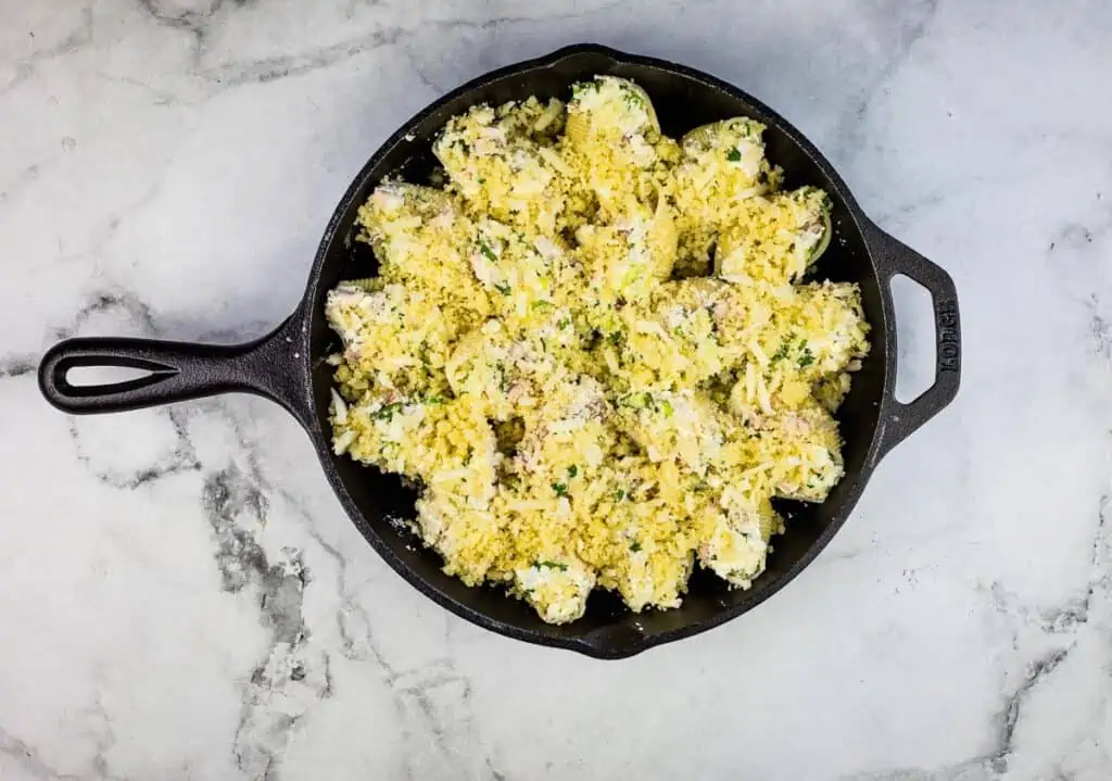 Turkey stuffed shells with pesto in the pan with the topping on them.