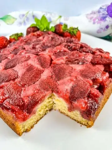 Strawberry Upside Down Cake on a plate with a slice cut out of it.