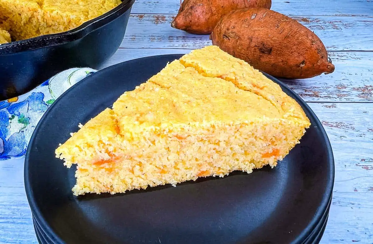 A piece of cornbread on a plate next to a few potatoes.