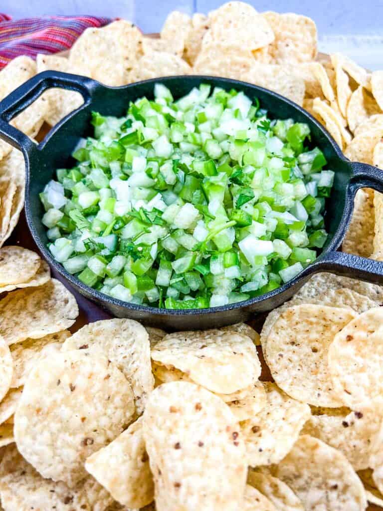 Tomatillo Pico de Gallo in a black dish with tortilla chips around it.