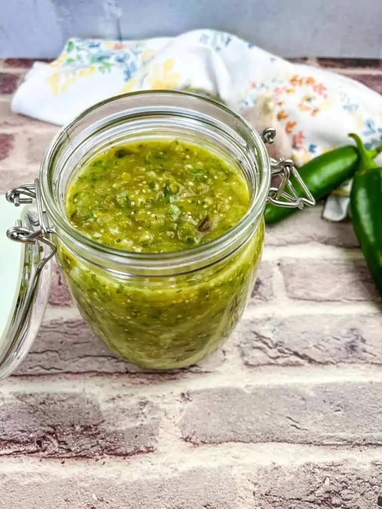 Creamy tomatillo sauce in a jar with jalapenos in the background.