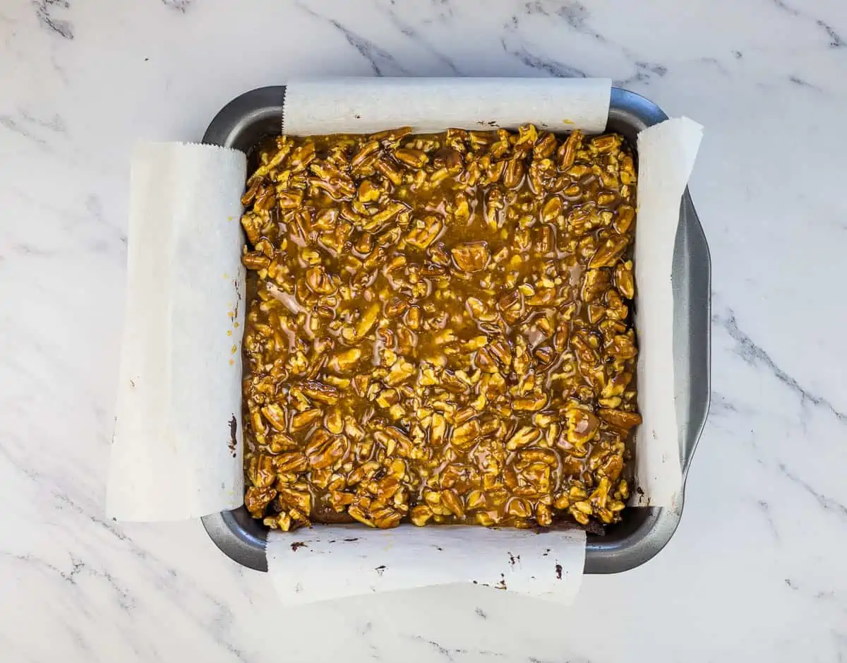 Pecan caramel mixture on top of brownies in a pan.