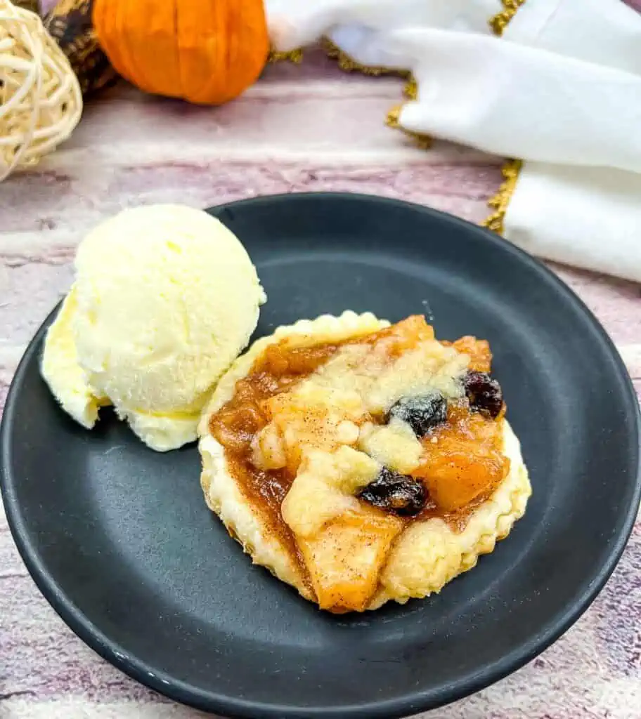 An apple-cranberry puff pastry tart on a black plate with a scoop of ice cream.