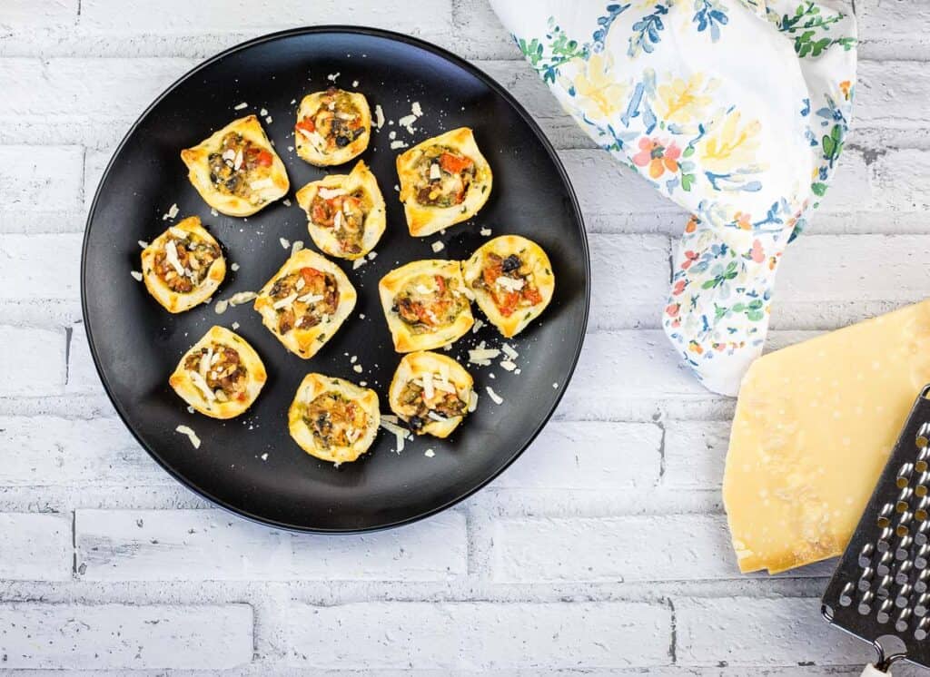 A top-down shot of Bacon and Mushroom Tartlets on a black plate.