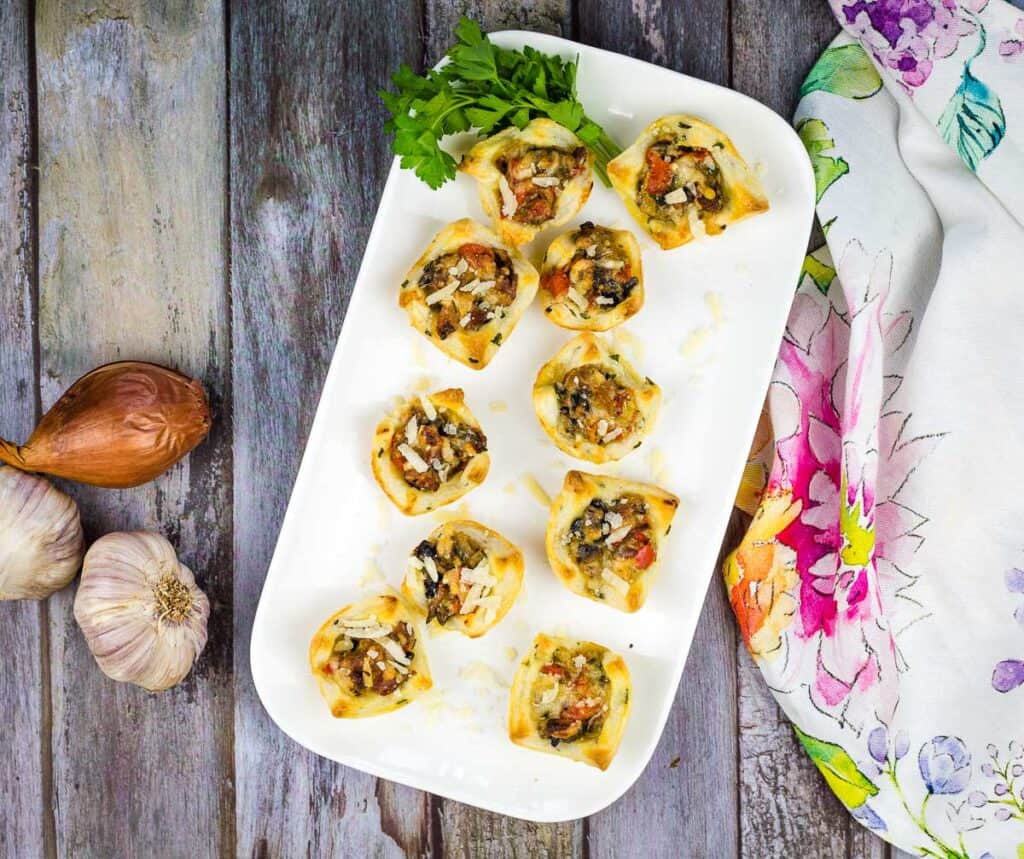 A top-down shot of Bacon and Mushroom Tartlets on a white platter.