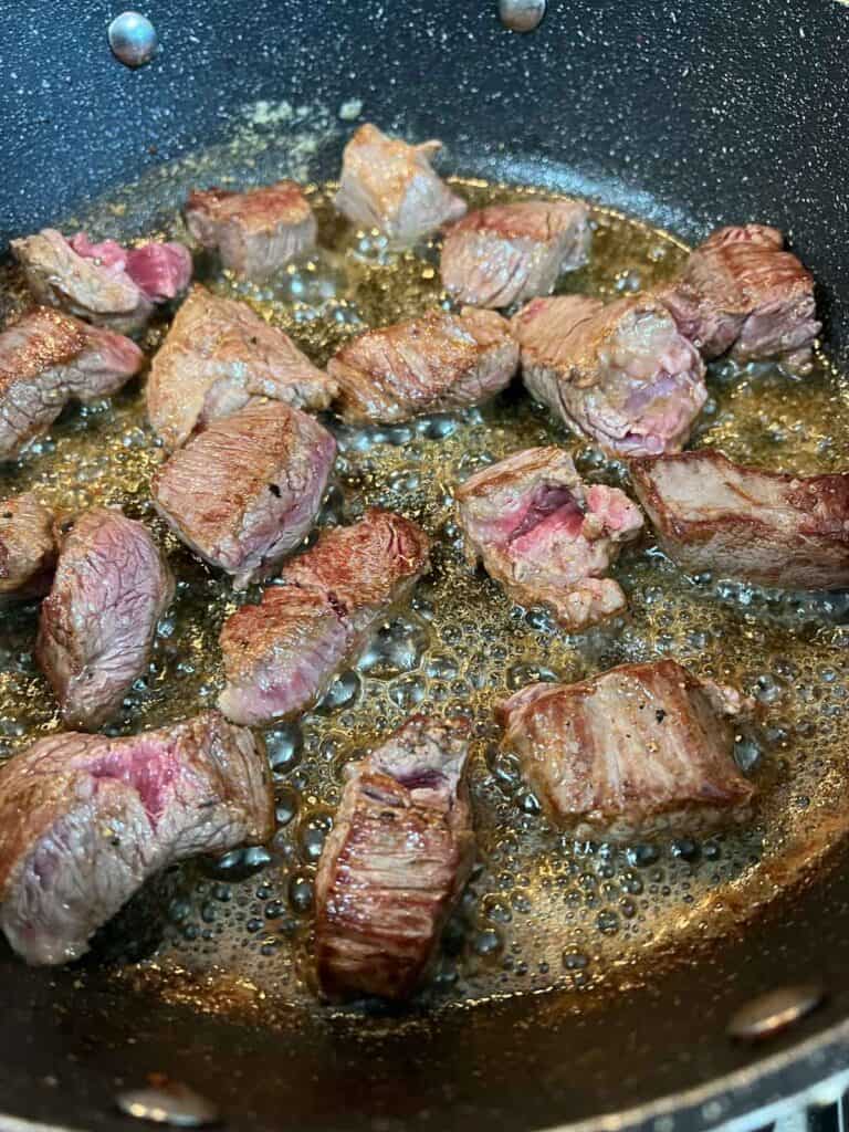 Browning the seasoned beef in butter and oil.