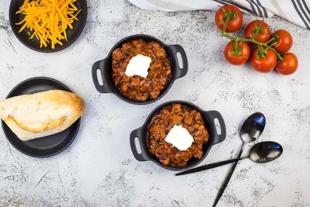 A top-down shot of smoked brisket chili in two bowls. Bread and cheese are on the side.